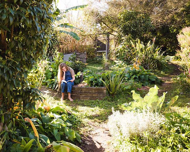 Maia sitting in a thriving permaculture garden
